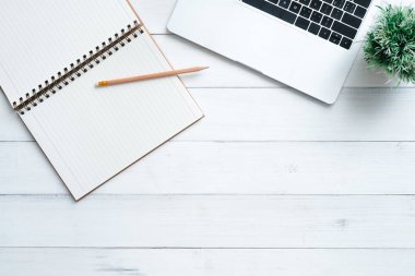 En az çalışma alanı - yaratıcı düz fotoğraf çalışma masası yatıyordu. Beyaz ahşap arka plan üzerinde bitki ve görünümü ofis büro dizüstü bilgisayar ile alay dizüstü kadar top. Kopya alanı, düz yatıyordu fotoğraf ile Üstten Görünüm