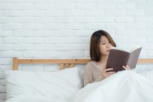 stock image Lifestyle happy young Asian woman enjoying lying on the bed reading book pleasure in casual clothing at home. Relaxing lifestyle woman concept.