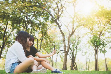 Parkta birlikte eğleniyor ve bir selfie alarak iki güzel mutlu genç Asyalı kadınlar arkadaş. Gülümseyen ve smartphone vasıl bakarak mutlu hipster genç Asyalı kızlar. Yaşam tarzı ve dostluk kavramları.
