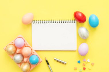 Düz renkli Paskalya yortusu yumurta pastel renkler bileşiminde boyalı üstten görünüm yatıyordu ve boş defter sarı pastel renk arka plan üzerinde boya fırçası ile alay. Paskalya günü arka plan üstten görünüm kopya alanı ile