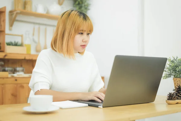 Kaunis nuori hymyilevä aasialainen nainen työskentelee kannettavan tietokoneen kanssa kotona toimistotiloissa. Liikenainen työskentelee kotoa kannettavan tietokoneen kirjoittaminen näppäimistöllä. Kotona viihtyminen . — kuvapankkivalokuva