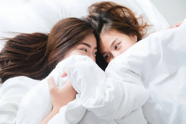 Beautiful young asian women LGBT lesbian happy couple hugging and smiling while lying together in bed under blanket at home. Funny women after wake up. LGBT lesbian couple together indoors concept. — Stock Photo, Image