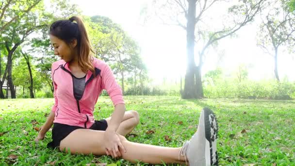 健康な若いアジア女性は公園でエクササイズします 朝のトレーニング トレーニングを行う若い女性に合います 若い幸せなアジア女は実行中のトレーニングの後 公園でストレッチします 運動屋外コンセプト — ストック動画