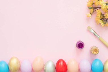 Düz yatıyordu üstten görünüm renkli Paskalya yortusu yumurta pastel renkler kompozisyon ve bahar çiçekleri pembe pastel renkli arka plan üzerinde boya fırçası ile boyanmış. Paskalya günü arka plan üstten görünüm kopya alanı ile.