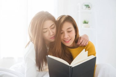 Yatakta kitap birlikte evde yatak odasında pencere yakınındaki okuma oturan güzel genç Asyalı kadınlar Lgbt lezbiyen mutlu çift. LGBT lezbiyen birlikte kapalı kavramı çift. Evde güzel vakit.