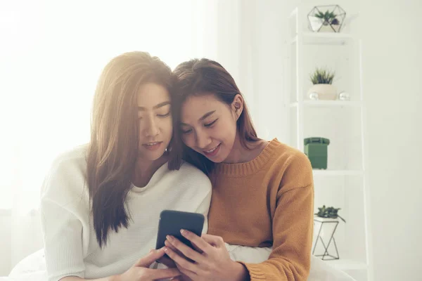 Vackra unga asiatiska kvinnor hbt-lesbisk lyckliga paret sitter på sängen kram och använda telefon grupp sovrum hemma. HBT-lesbisk par tillsammans inomhus koncept. Tillbringa trevliga tid hemma. — Stockfoto