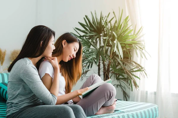 Belle giovani donne asiatiche lesbiche LGBT felice coppia seduta sul divano lettura libro insieme vicino alla finestra in soggiorno a casa. LGBT coppia lesbica insieme indoor concetto. Trascorrere del bel tempo a casa — Foto Stock