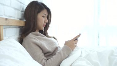 Mutlu Asyalı kadınlar akıllı telefon sabah yatakta kullanıyorsunuz. Asyalı kadın yatakta smartphone ile sosyal uygulamalar kontrol. Gülümseyen kadın evde cep telefonu ile net sörf. Telefon bağımlısı kavramı.