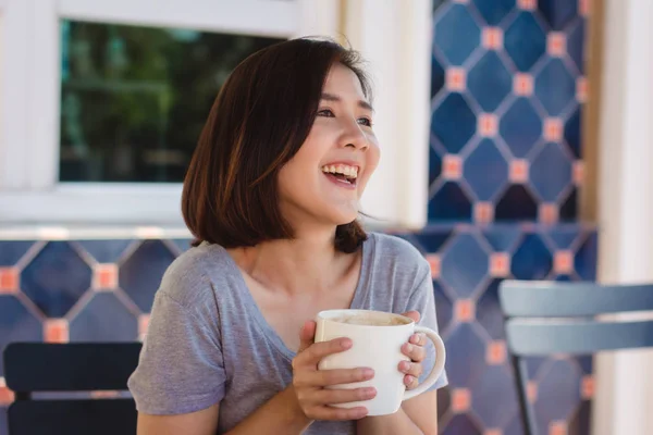 Potret wanita bisnis Asia muda yang bahagia dengan cangkir di tangan minum kopi di pagi hari di kafe. Wanita Asia mengekspresikan emosi santai di kafe atau kedai kopi. Wanita makanan dan minum konsep kafe . — Stok Foto