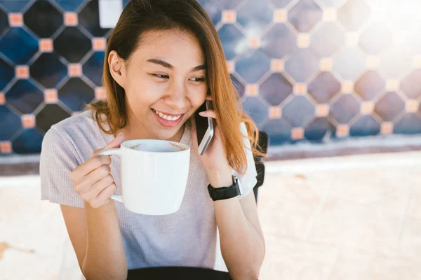 Wanita bisnis tersenyum asia yang bahagia menggunakan ponsel yang bisa bicara duduk di kafe dan memegang secangkir kopi. Indah ceria perempuan asia di kafe berbicara di telepon dan tersenyum sambil menikmati kopi . — Stok Foto