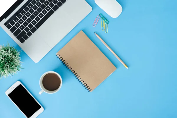 Office desk working space - Flat lay top view copy space of working space with laptop, blank notebook, coffee and smartphone placing on blue pastel copy space. Pastel blue background space concept.