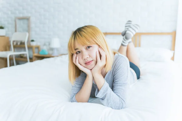 Portrett av vakker ung asiatisk kvinne på sengen hjemme om morgenen. Munter asiatisk kvinne i en komfortabel genser og smiler på sengen sin. Avslappende rom. livsstil asiatisk kvinne som hjemmebegrep . – stockfoto