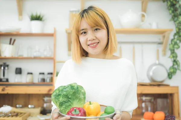 Smilende asiatisk vakker kvinne som sitter på kjøkkenet og holder en salatbolle. Ung, lykkelig kvinne som spiser sunn salat med friske ingredienser til en sunn kropp . – stockfoto
