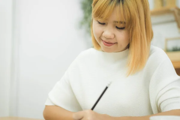 Vakker, ung, smilende asiatisk kvinne som jobber med laptop mens hun sitter i stua hjemme. Asiatisk forretningskvinne som jobber på hjemmekontoret. Nyter tid hjemme . – stockfoto