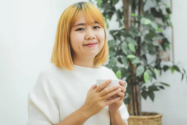 Houkutteleva kaunis aasialainen nainen nauttii lämmintä kahvia keittiössä kotonaan. Aasialainen nainen yllään mukava pusero tilalla kuppi kahvia. elämäntapa Aasia nainen kotona käsite . — kuvapankkivalokuva