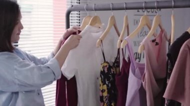 Asyalı kadın elbisesi alışveriş. Alışveriş giyim giyim mağazasında kapalı Ray üzerinde bakarak. Güzel mutlu gülümseyen Asyalı kadın modeli. Orta atış.
