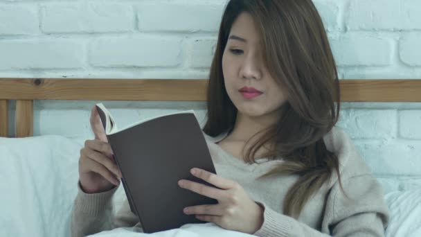生活愉快的年轻的亚洲妇女享受躺在床上看书休闲服装在家中的乐趣 放松生活方式妇女概念 — 图库视频影像