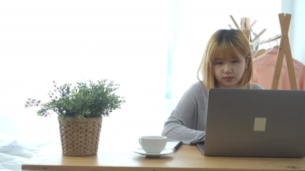 美丽的年轻微笑的妇女工作在笔记本电脑 而享受喝着温暖的咖啡坐在客厅在家里 在家里享受时光 在她的家庭办公室工作的亚洲商人妇女 — 图库视频影像