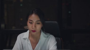 Millennial genç Çinli iş kadını küçük modern ofisteki toplantı odasında dizüstü bilgisayardaki proje araştırma sorunuyla geç saatlere kadar çalışıyor. Asyalıların mesleki tükenme sendromu. Yavaş çekim