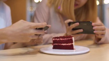 Neşeli genç Asyalı arkadaş kahve dükkanında fotoğraf yemek ve kek yerken telefon kullanıyor. Lokantada ya da kafede birlikte iki neşeli ve çekici Asyalı bayan. Tatil aktivitesi, ya da modern yaşam tarzı konsepti.