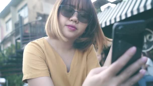 屋外カフェで携帯電話を使用して観光アジアの女性 Snsで友達とSnsでSnsやテキストメッセージをチェックしながら旅の休日旅行を楽しむ日本の若いアジアの女の子 — ストック動画