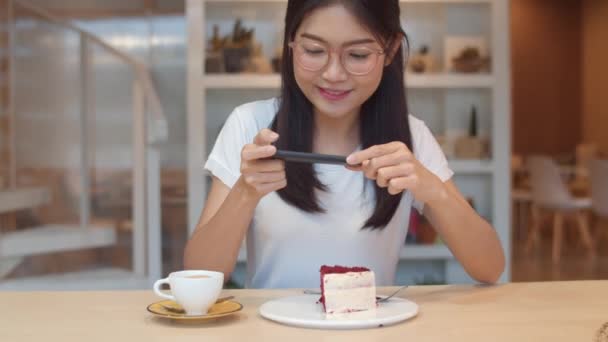 ブロガーアジア系のフレンドリーな女性のインフルエンサーが夜カフェでケーキを食べる 美しい若い女性が大学のキャンパスでソーシャルメディアで彼女の食べ物のアップロードの写真を撮る技術携帯電話を使用して楽しいリラックス — ストック動画