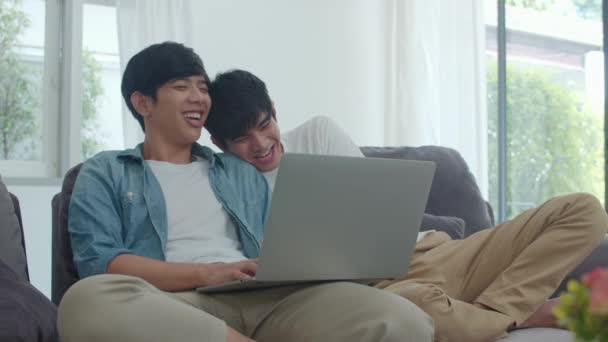 現代の家庭でコンピュータのラップトップを使用して若いゲイのカップル アジアのLgbtqの男性は家のコンセプトでリビングルームでソファに横たわっている間 一緒にインターネットで技術を見て映画を使用して楽しいリラックス — ストック動画