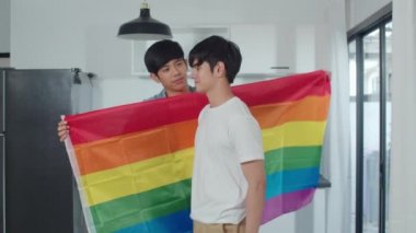 Asyalı eşcinsel çift evde ayakta ve sarılma odasında. Genç yakışıklı Lgbtq + erkekler mutluluğu öpüyor birlikte dinlenin modern mutfakta romantik vakit geçirin sabah konseptinde gökkuşağı bayrağıyla.