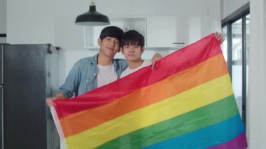 Genç Asyalı eşcinsel çift evde gökkuşağı bayrağı gösterdikleri için mutlu. Asya Lgbtq + erkekler rahatlar dişlek gülümseme kameraya bakarken modern mutfakta sarılmak sabah konsepti.