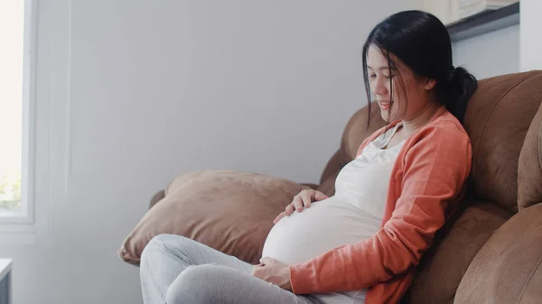 Młoda Azjatka w ciąży, trzymająca brzuch przy dziecku. Mama czuje szczęśliwy uśmiech pozytywny i spokojny podczas dbać o dziecko, ciąża leży na kanapie w salonie koncepcja domu. — Zdjęcie stockowe