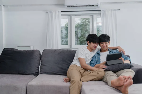 Pareja gay joven usando tableta en casa. Asiático LGBTQ + hombres feliz relajarse divertido usando tecnología viendo película en internet juntos mientras que el sofá acostado en sala de estar concepto . —  Fotos de Stock