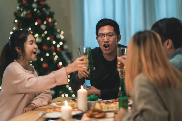 Hyvää joulua ja onnellista uutta vuotta! Nuoret ystävät syövät päivällistä kotona. Aasialaiset perhejuhlat oluella ja pizzalla lähellä joulukuusi talossa yöllä. Juhlaloma ja yhdessäolo . — kuvapankkivalokuva