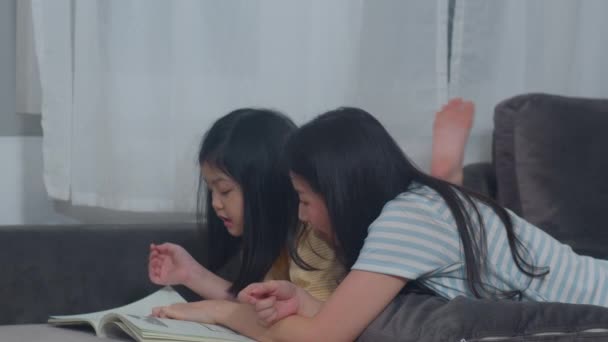 アジアの中年女性は娘に読書を教える本は自宅でリラックスした自由な時間をお楽しみください ライフスタイルの母親と子供の幸せ楽しい夜のコンセプトで現代の家のリビングルームで一緒に時間を過ごす — ストック動画