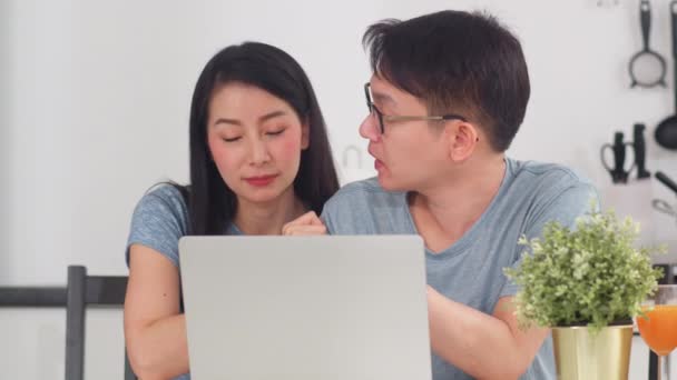 若いアジアのカップルは自宅でラップトップでオンラインショッピングをお楽しみください 朝のコンセプトで家のモダンなキッチンで朝食を食べた後のライフスタイルの若い夫と妻の幸せな購入Eコマース — ストック動画