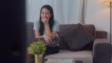 Asyalı orta yaşlı kadın evde dinlenerek boş zamanın tadını çıkarıyor. Yaşam tarzı kızı mutlu bir eğlence filmi izler ve modern evdeki oturma odasında gece konseptini seyreder..