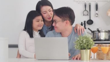 Genç Asyalı aile evde birlikte dizüstü bilgisayar kullanmaktan hoşlanıyor. Yaşam tarzı, genç karı, koca ve kız mutlu bir kucaklaşma ve sabah konseptiyle modern mutfakta kahvaltı ettikten sonra oynaşma..