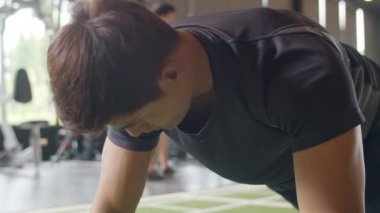 Yakışıklı genç atlet Asyalı adam fitness sınıfında şınav çekerek yağ yakma egzersizi yapıyor. Sporcu eğlencesi, fonksiyonel eğitim, spor yapan insanlar, sağlıklı yaşam tarzı konsepti..
