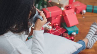 Asyalı kadınlar Noel festivalini kutluyor. Kadın genç kanepede yatan Noel ağacı yakınında kahvaltı içki kahve sahip mutlu dinlenmek evde oturma odasında xmas kış tatilleri keyfini çıkarın.
