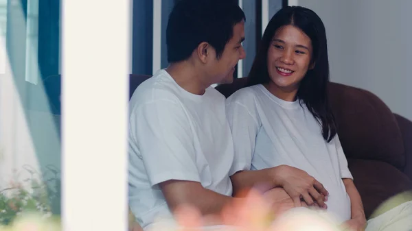 Jeune asiatique enceinte couple homme toucher sa femme ventre parler avec son enfant. Maman et papa se sentent heureux souriant paisible tout en prenant soin bébé, grossesse couchée sur le canapé dans le salon à la maison concept. — Photo