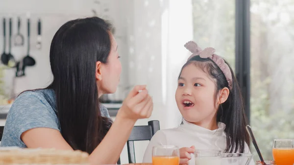 La familia japonesa asiática desayuna en casa. Asiática mamá e hija feliz hablando juntos mientras come pan, beber jugo de naranja, cereales copos de maíz y leche en la mesa en la cocina moderna por la mañana . — Foto de Stock