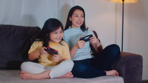 Νεαρή ασιατική οικογένεια και η κόρη παίζουν παιχνίδια στο σπίτι το βράδυ. Κορεάτισσα μητέρα με μικρό κορίτσι χρησιμοποιώντας joystick αστεία ευτυχισμένη στιγμή μαζί στον καναπέ στο σαλόνι. Η αστεία μαμά και το υπέροχο παιδί διασκεδάζουν. — Φωτογραφία Αρχείου
