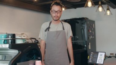 Genç Asyalı garson baristanın portresi. Elinde kahve fincanı var. Şehir kafesinde kendini mutlu hissediyor. Asya 'daki küçük işletme sahibi çocuk rahatla dişlek gülümseme kahve dükkanında kameraya bakıyor..