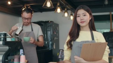 Portre genç Asyalı çift barista şehir kafesinde menüden memnun. Küçük işletme sahibi Koreli arkadaşlar rahatlayın dişlek gülümseme kahve dükkanının tezgahında kameraya bakıyor.