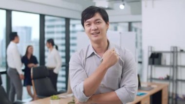 Modern ofis işyerinde kollarını kavuşturarak kameraya bakıp gülümseyen başarılı, yakışıklı yönetici iş adamının portresi. Genç Asyalı adam çağdaş toplantı odasında duruyor..