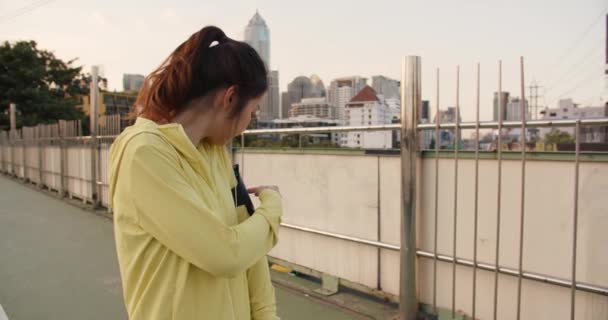 年轻美丽的亚洲女运动员在城市跑步时 用智能手机听音乐 一大早 韩国少女穿着运动服在走道桥上 — 图库视频影像