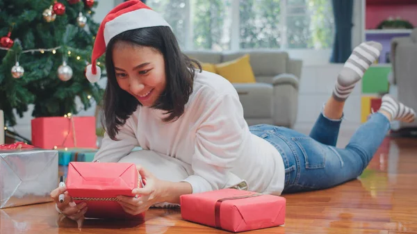 Asian women celebrate Christmas festival. Female teen wear sweater and santa hat relax happy write a wish on gift near Christmas tree enjoy xmas winter holidays together in living room at home.
