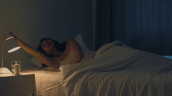 Hermosa mujer joven asiática durmiendo acogedora en su dormitorio. La mano femenina india apagando el interruptor de luz cerca de la cama en la habitación en casa en la noche lista para dormir. Dulces sueños y concepto de relajación . —  Fotos de Stock