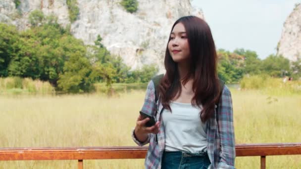 年轻快乐的亚洲女旅行家 背着背包在山湖边自拍 韩国女孩喜欢用手机自拍 享受徒步旅行的乐趣 生活方式旅行和放松的概念 — 图库视频影像