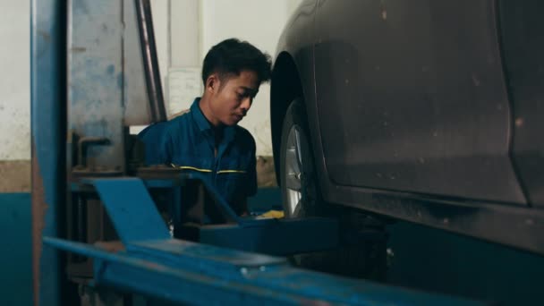 修理サービスステーションで解除された自動車の車のエンジンの専門的な車の整備士のねじ込み詳細 夜のメカニズムガレージで均一な固定車の熟練したアジアの男 4Kスローモーションショット — ストック動画