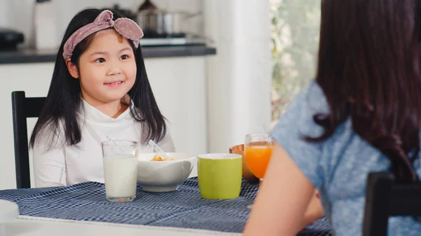 La familia japonesa asiática desayuna en casa. Mamá asiática, papá e hija se sienten felices hablando juntos mientras comen pan, cereales en copos de maíz y leche en un tazón en la mesa de la cocina por la mañana. . — Foto de Stock